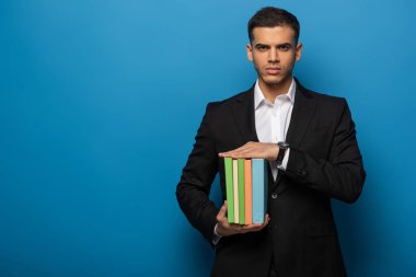Yakışıklı iş adamı elinde mavi arka planda renkli kitaplar tutuyor.