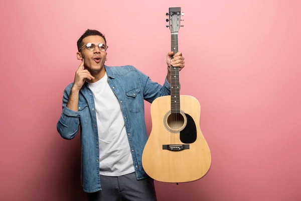 Schockierter Mann Mit Finger Wange Und Akustikgitarre Auf Rosa Hintergrund — Stockfoto