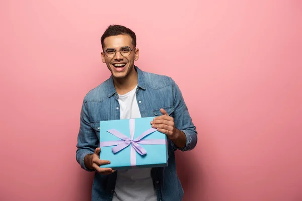 快乐的男人对着相机微笑 拿着粉色背景的礼品盒 — 图库照片