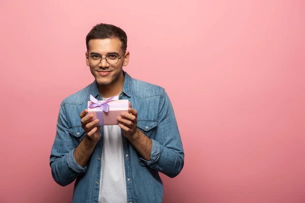 Νεαρός Άνδρας Κοιτάζοντας Κάμερα Ενώ Κρατώντας Κουτί Δώρου Ροζ Φόντο — Φωτογραφία Αρχείου