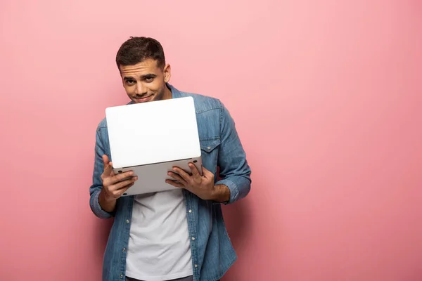 Νεαρός Άνδρας Χαμογελά Στην Κάμερα Ενώ Κρατά Laptop Ροζ Φόντο — Φωτογραφία Αρχείου