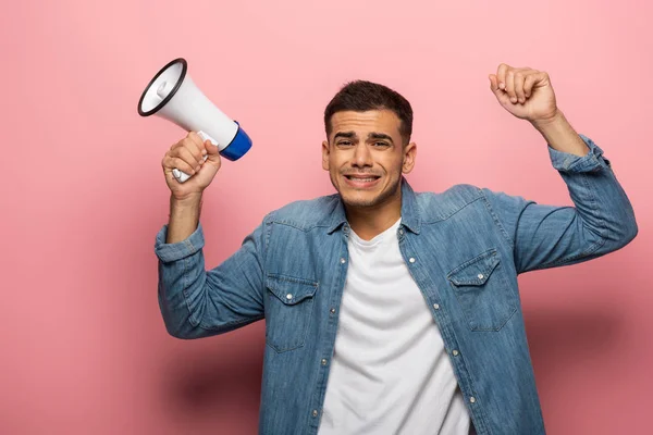 Upset man looking at camera while holding loudspeaker on pink background