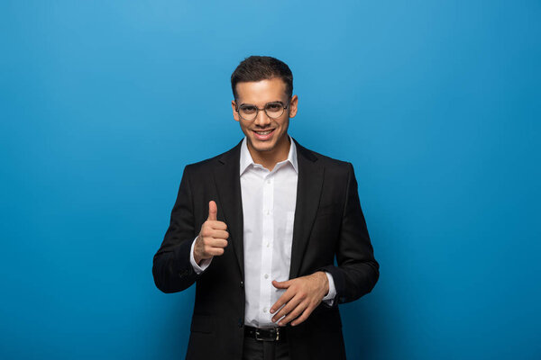 Улыбающийся бизнесмен показывает большой палец вверх жестом на синем фоне
