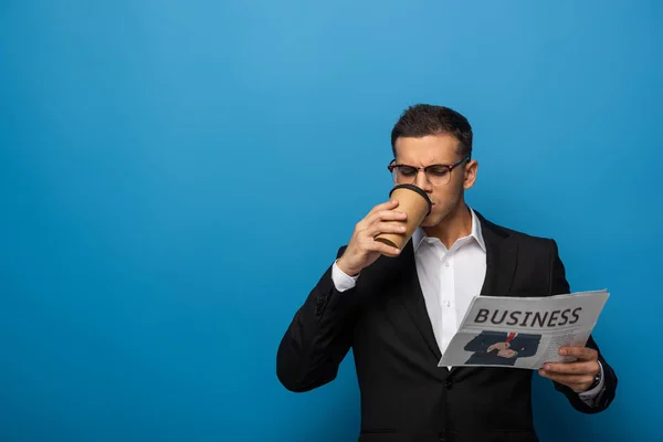 ブルーを背景に新聞を読むためにコーヒーとハンサムなビジネスマン — ストック写真