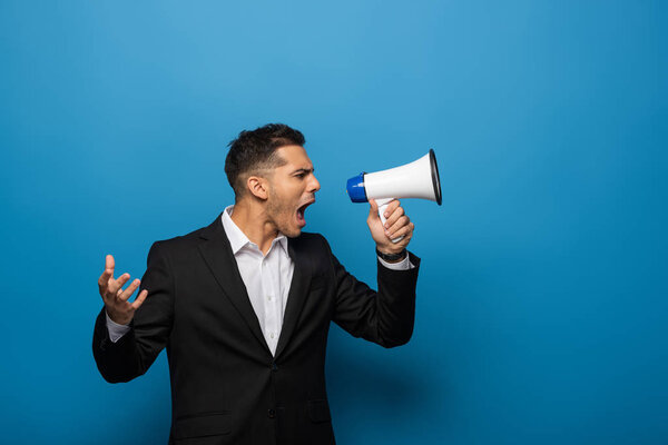 Вид сбоку бизнесмена, кричащего в громкоговоритель на голубом фоне
