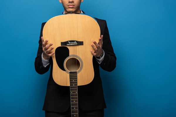 Обрезанный вид бизнесмена, держащего акустическую гитару на синем фоне

