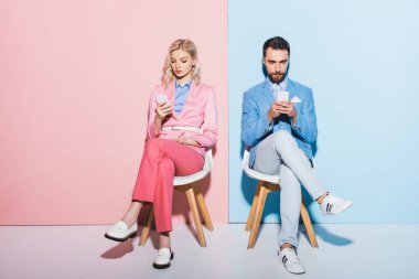 Pembe ve mavi arka planda akıllı telefon kullanan çekici kadın ve yakışıklı erkek. 