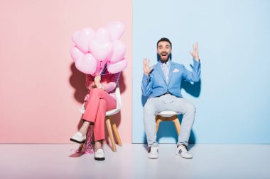 Kadın balon tutuyor ve elleri pembe ve mavi arka planda olan şok olmuş bir adam. 