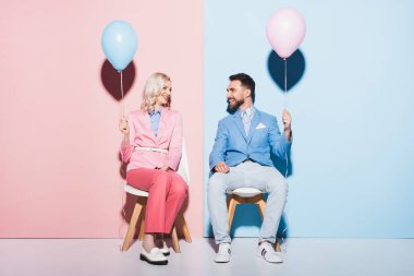 gülümseyen kadın ve yakışıklı adam pembe ve mavi arka planda balonlar tutuyorlar. 
