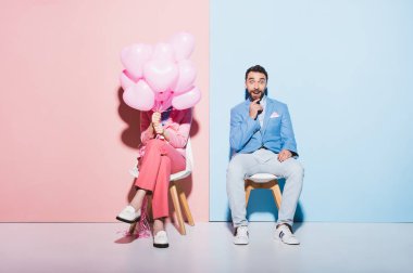 Kadın balon tutuyor ve şok olmuş adam pembe ve mavi arka planda 