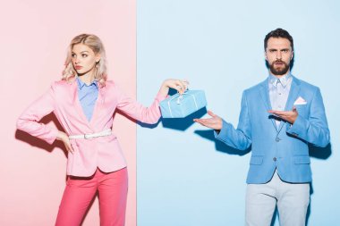 Hediye tutan üzgün kadın ve elleri pembe ve mavi arka planda olan şok olmuş adam. 