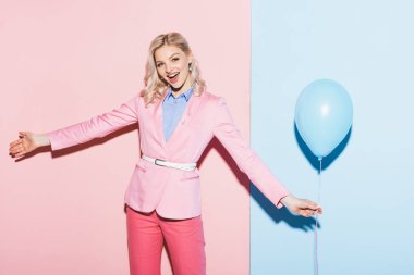 Gülümseyen kadın pembe ve mavi arka planda balon tutuyor. 