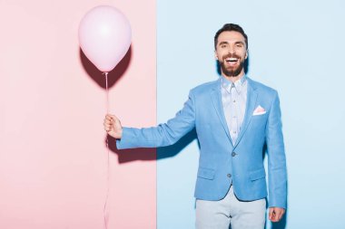 Mavi ve pembe arka planda balon tutan yakışıklı ve gülümseyen adam. 