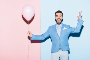 Mavi ve pembe arka planda balon tutan yakışıklı ve gülümseyen adam. 