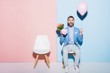 Yakışıklı ve gülümseyen adam elinde balon, hediye ve buket mavi ve pembe arka planda 