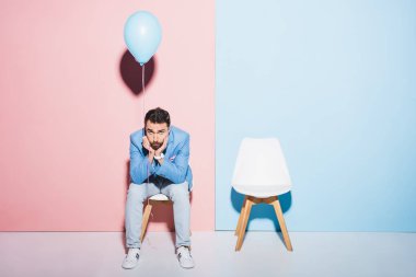Yakışıklı ve üzgün adam mavi ve pembe arka planda balon tutuyor. 