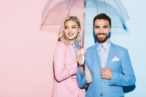 笑顔の女性とハンサムな男で傘を持ってピンクと青の背景 — ストック写真