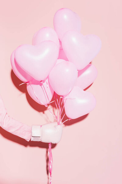 cropped view of woman in boxing glove holding balloons on pink background 