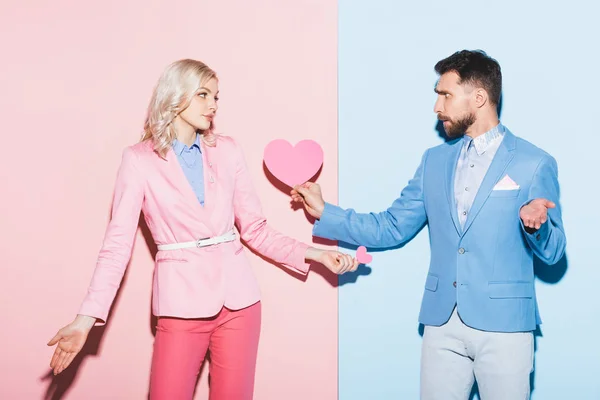 悲しい女とハンサムな男がピンクと青の背景にハート型のカードを持っている — ストック写真