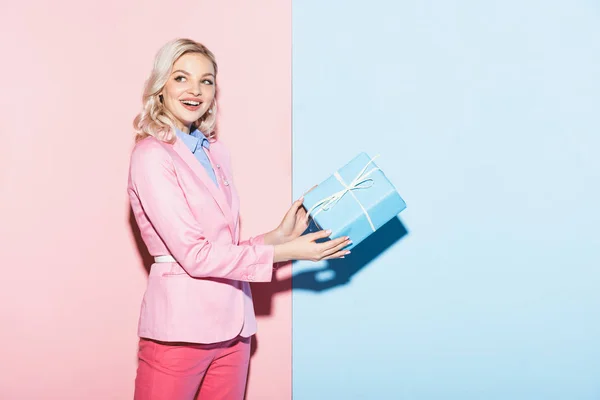 Smiling Woman Holding Gift Box Pink Blue Background — Stock Photo, Image