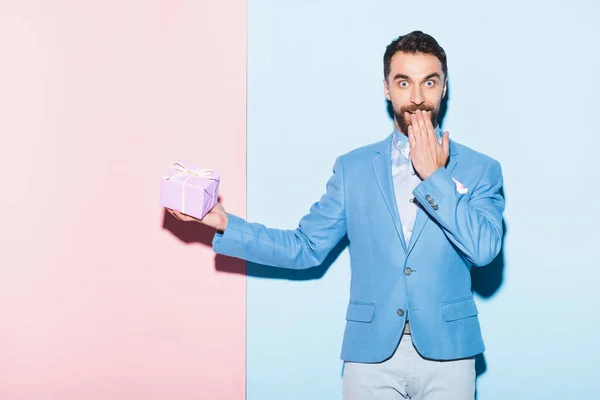 Handsome Shocked Man Holding Gift Blue Pink Background — Stock Photo, Image