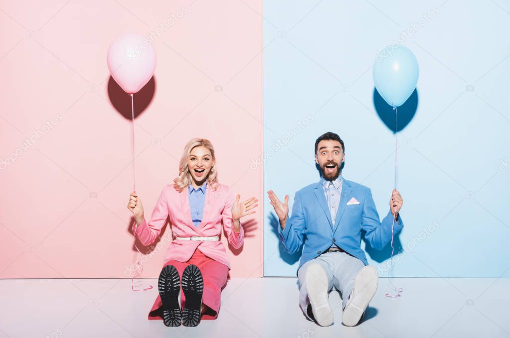shocked woman and handsome man holding balloons on pink and blue background 