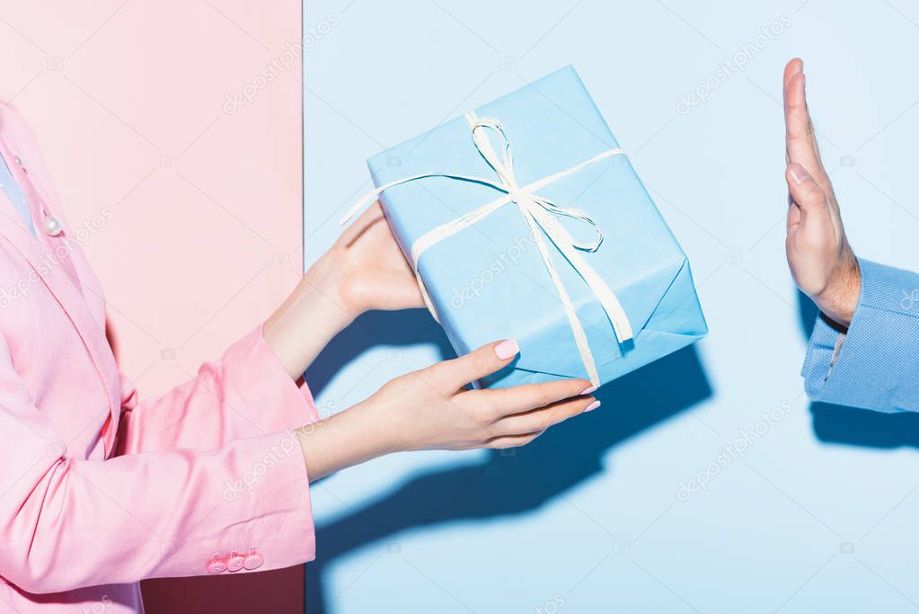 cropped view of woman giving present to man on pink and blue background 