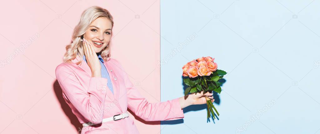 panoramic shot of smiling woman holding bouquet on pink and blue background 