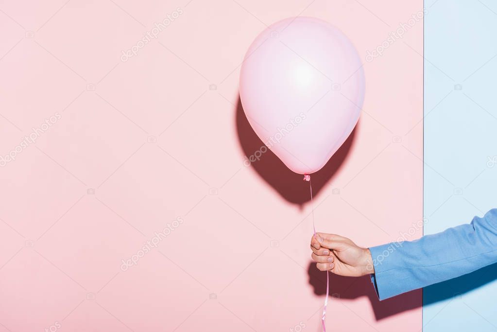 cropped view of man holding balloon on blue and pink background 