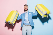 mosolygós férfi gazdaság utazási táskák rózsaszín és kék háttér 