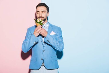 Gülümseyen adam pembe ve mavi arka planda buket kokusu alıyor. 