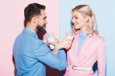 attractive woman and smiling man drinking cocktails on pink and blue background  clipart