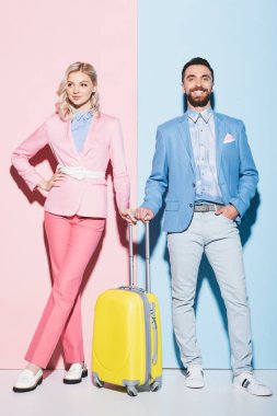 Gülümseyen kadın ve pembe ve mavi arka planda seyahat çantası taşıyan yakışıklı adam. 