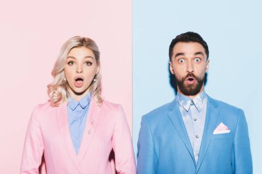 shocked woman and handsome man looking at camera on pink and blue background  clipart