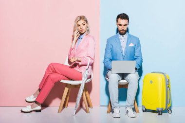 Akıllı telefonda konuşan bir kadın ve pembe ve mavi arka planda dizüstü bilgisayar kullanan yakışıklı bir adam. 