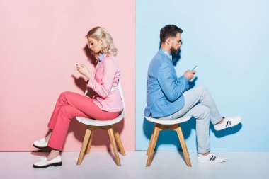 Pembe ve mavi arka planda akıllı telefon kullanan kadın ve yakışıklı adamın yan görüntüsü 
