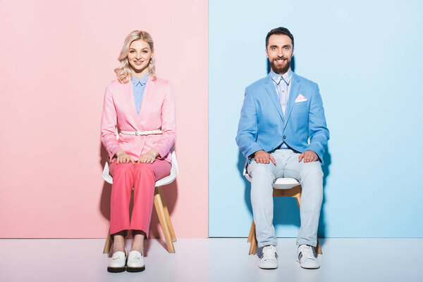 smiling woman and handsome man looking at camera on pink and blue background 