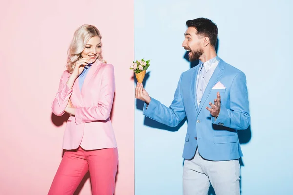 ピンクと青の背景を持つ魅力的な女性に花束を与えるショックを受けた男 — ストック写真