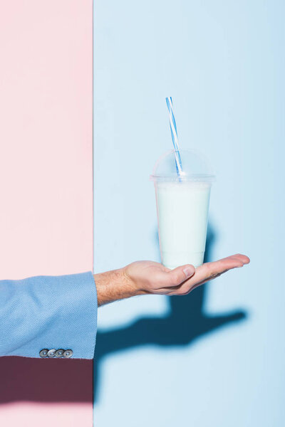обрезанный вид человека, держащего коктейль на розовом и синем фоне
 
