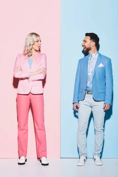 attractive woman sticking out tongue and smiling man looking at her on pink and blue background