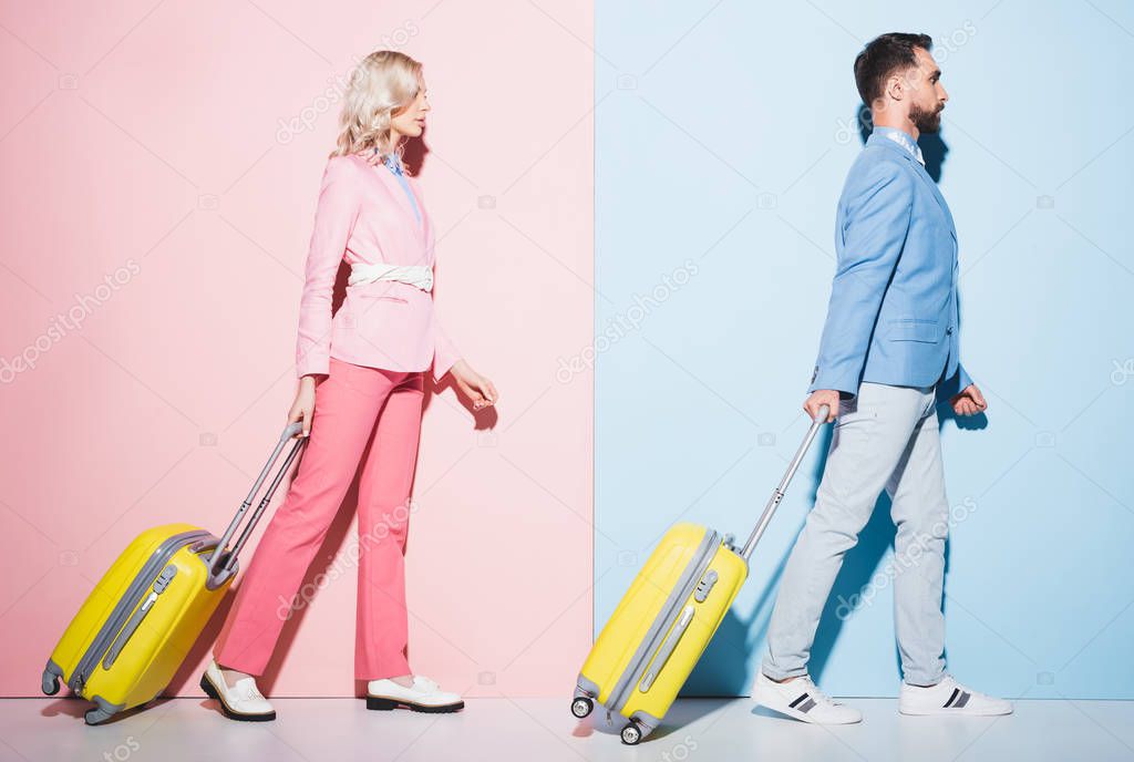 side view of attractive woman and handsome man walking with travel bags on pink and blue background 
