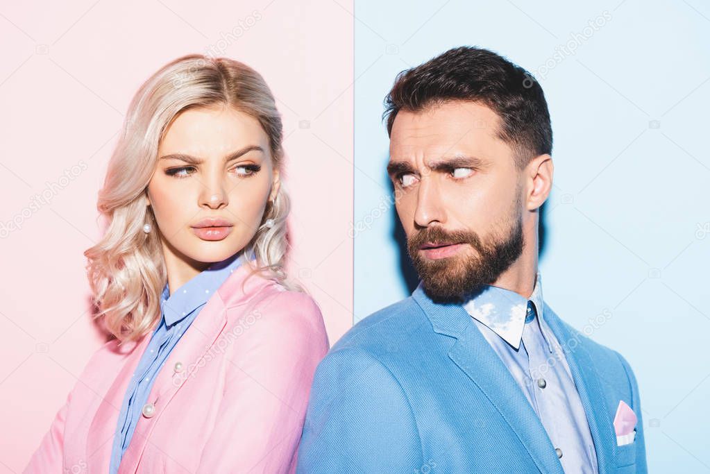 irritated woman and handsome man looking at each other on pink and blue background 