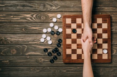 Dama tahtasının üstünde tahta zeminde dama oynayan kadın ve erkeğin kesikli görüntüsü