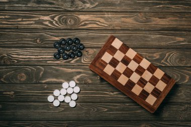 Top view of checkers beside chessboard on wooden background clipart