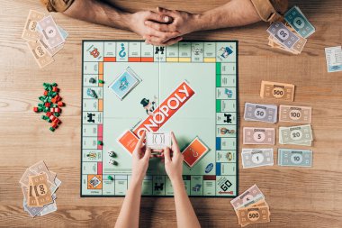 KYIV, UKRAINE - NOVEMBER 15, 2019: Cropped view of woman and man playing monopoly board game at table clipart
