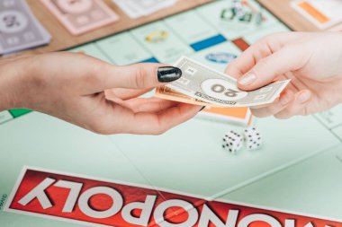 KYIV, UKRAINE - NOVEMBER 15, 2019: Cropped view of women holding toy currency while playing in monopoly  clipart