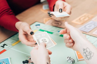 KYIV, UKRAINE - NOVEMBER 15, 2019: Cropped view of women with toy currency and cards playing in monopoly clipart