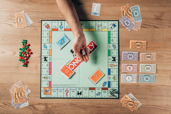 KYIV, UKRAINE - NOVEMBER 15, 2019: Cropped view of man holding dices with monopoly game on table