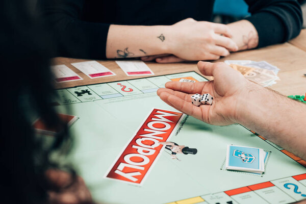 KYIV, UKRAINE - NOVEMBER 15, 2019: Cropped view of man and women playing in monopoly at table