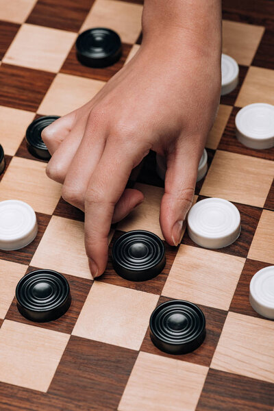 Обрезанный вид женщины, держащей черную шашку на деревянной шашке
